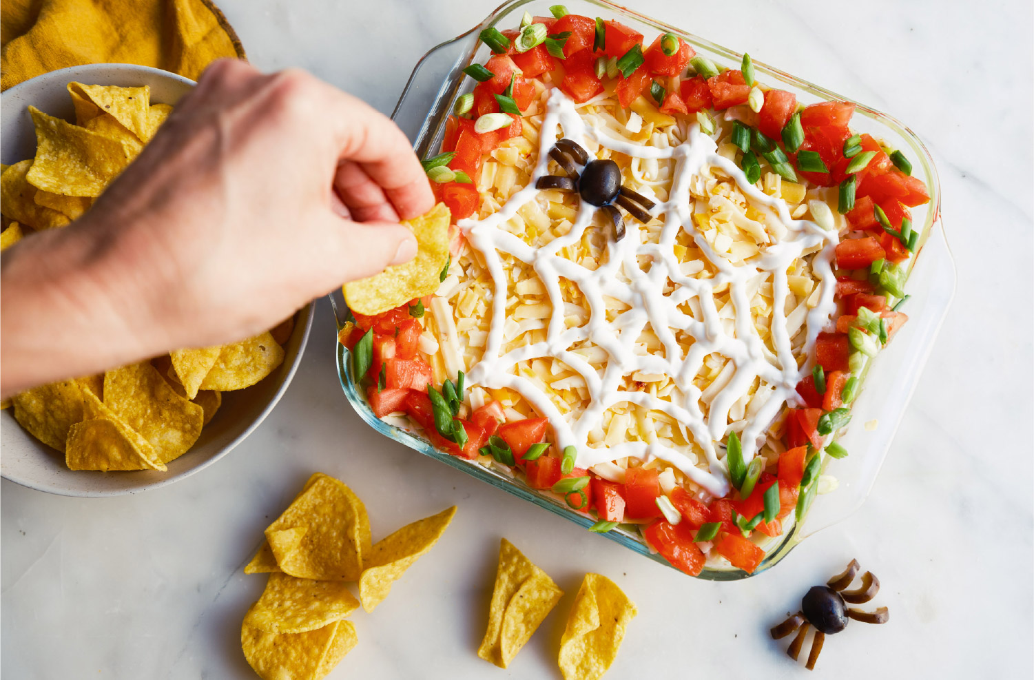 Halloween 7-Layer Dip with spiced American Lamb, cheese, tomatoes, green onions, and a sour cream spider-web design