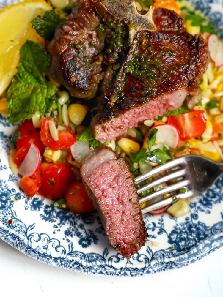 Medium rare lamb loin chop served with grilled corn salad and fresh vegetables