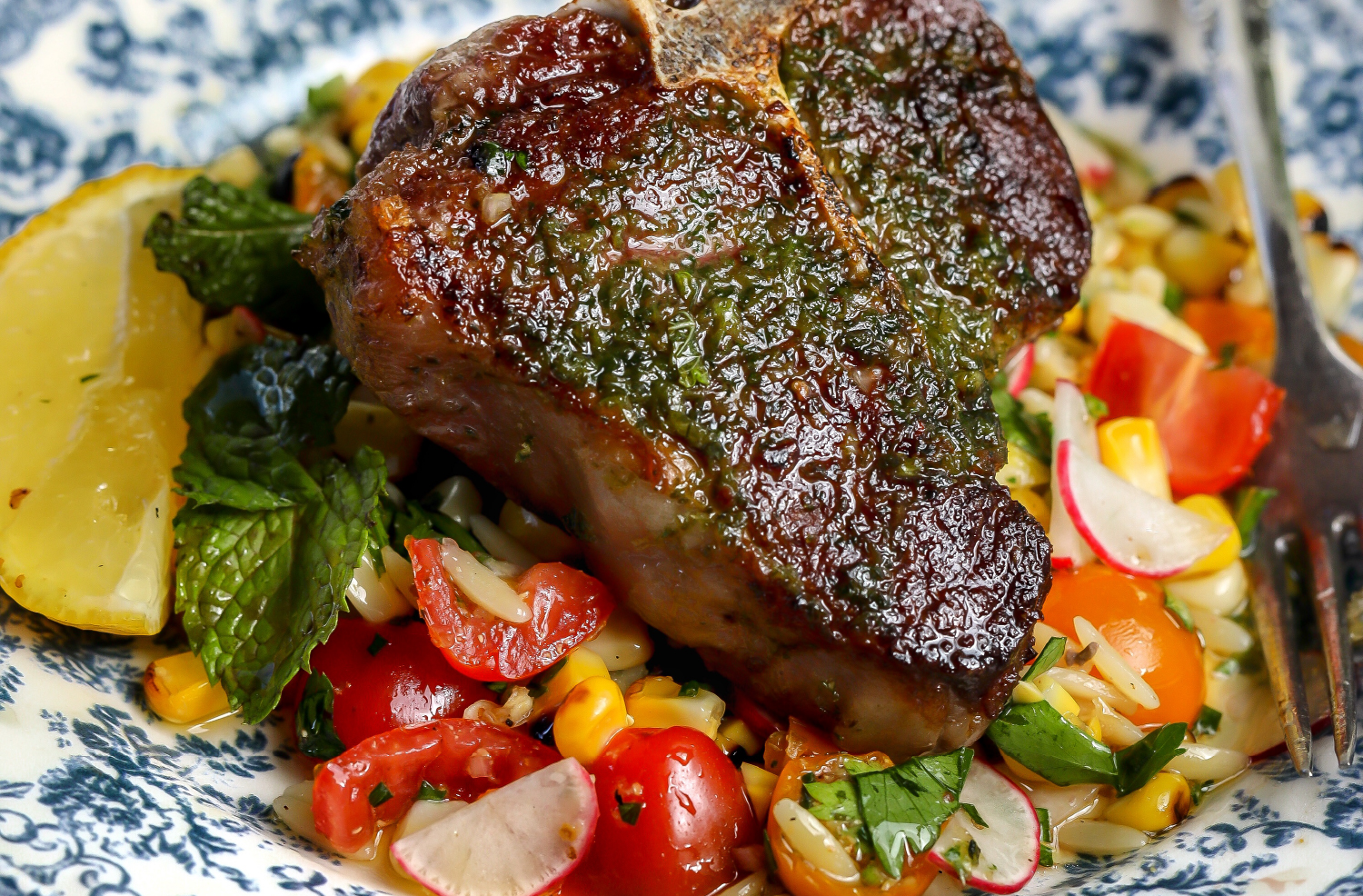 Lamb loin chops served over grilled corn salad with cherry tomatoes, radishes, fresh herbs, and lemon.