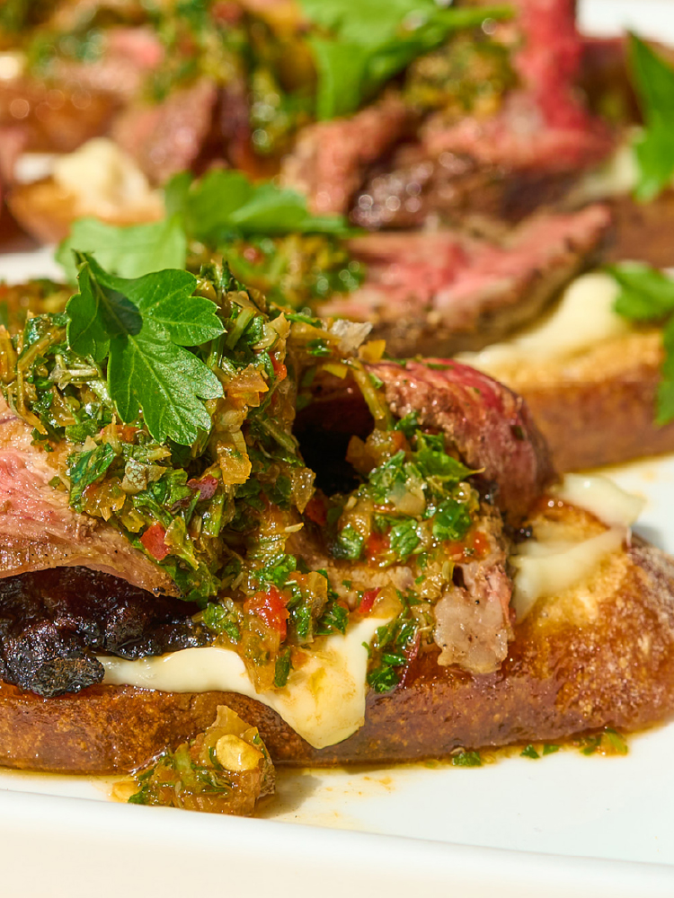 Platter of grilled lamb crostini with herb salsa verde and toasted baguette slices