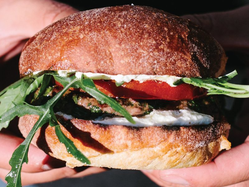 American lamb herb burger with whipped feta, grilled tomato, and arugula on a toasted bun