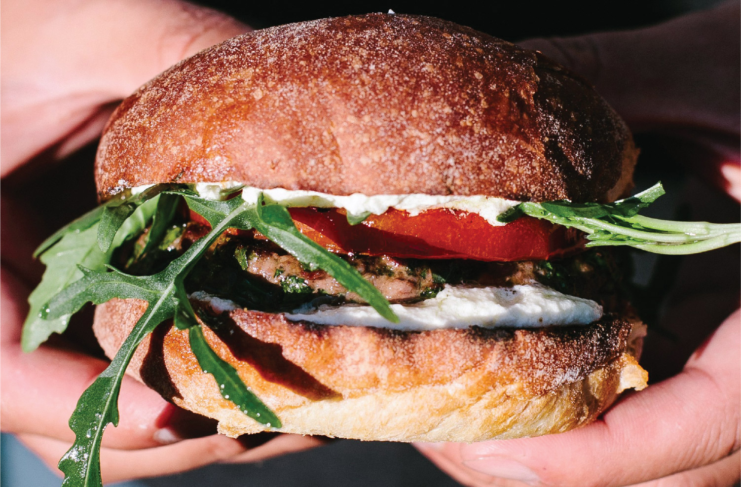 American lamb herb burger with whipped feta, grilled tomato, and arugula on a toasted bun