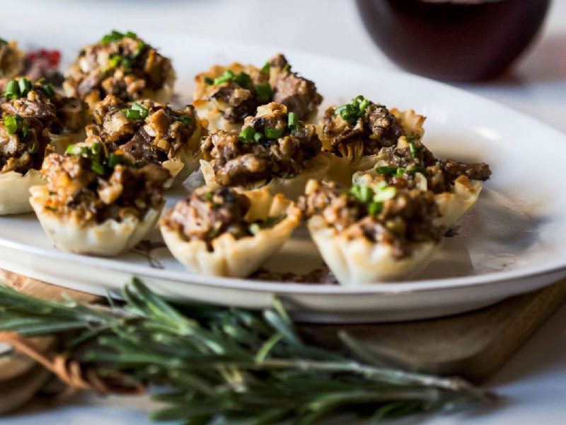 Mini lamb wellington bites in crispy filo shells arranged on a platter with fresh chives