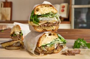 Stacked Slow-Cooked American Lamb Sandwiches filled with shredded lamb, charred onions, greens, and jalapeño aioli.