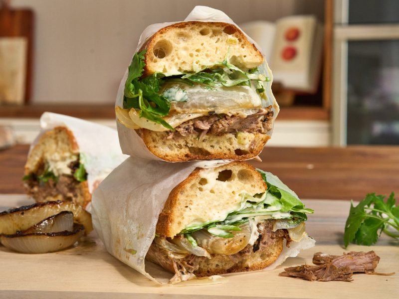 Stacked Slow-Cooked American Lamb Sandwiches filled with shredded lamb, charred onions, greens, and jalapeño aioli.