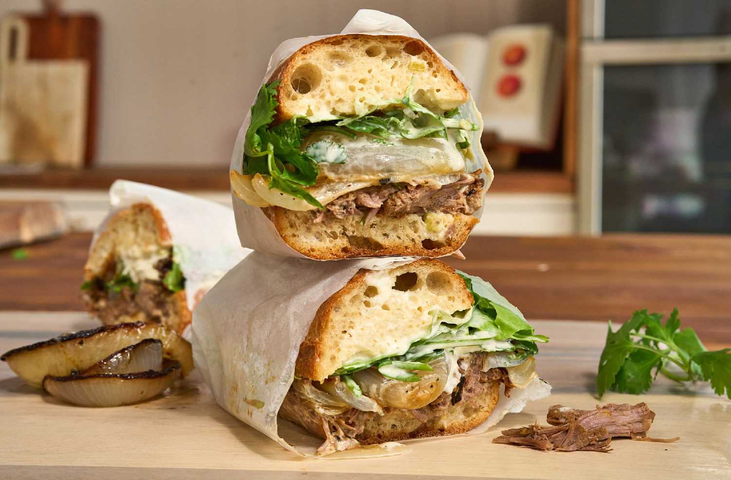 Stacked Slow-Cooked American Lamb Sandwiches filled with shredded lamb, charred onions, greens, and jalapeño aioli.