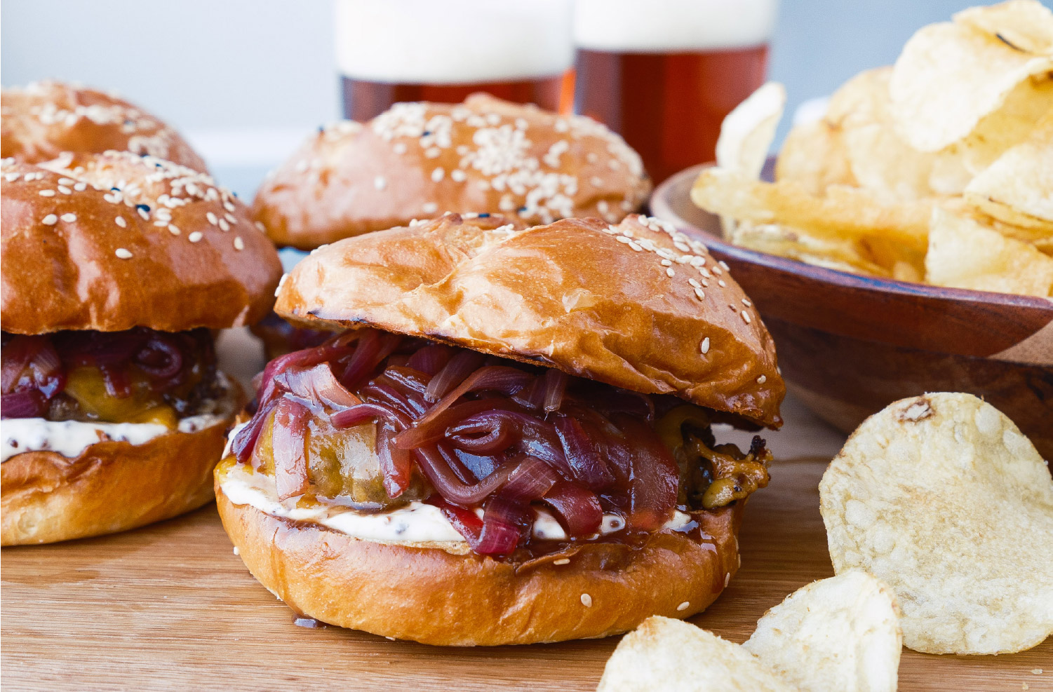 Lamb Smashburgers topped with melted cheese, sweet red onion jam, and mustard mayo on toasted sesame seed buns, served with potato chips.