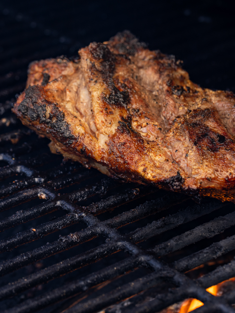Marinated American lamb grilling over open flame on a barbecue grill